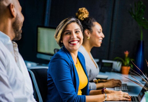 Woman investor smiling with coworker as they work on laptops